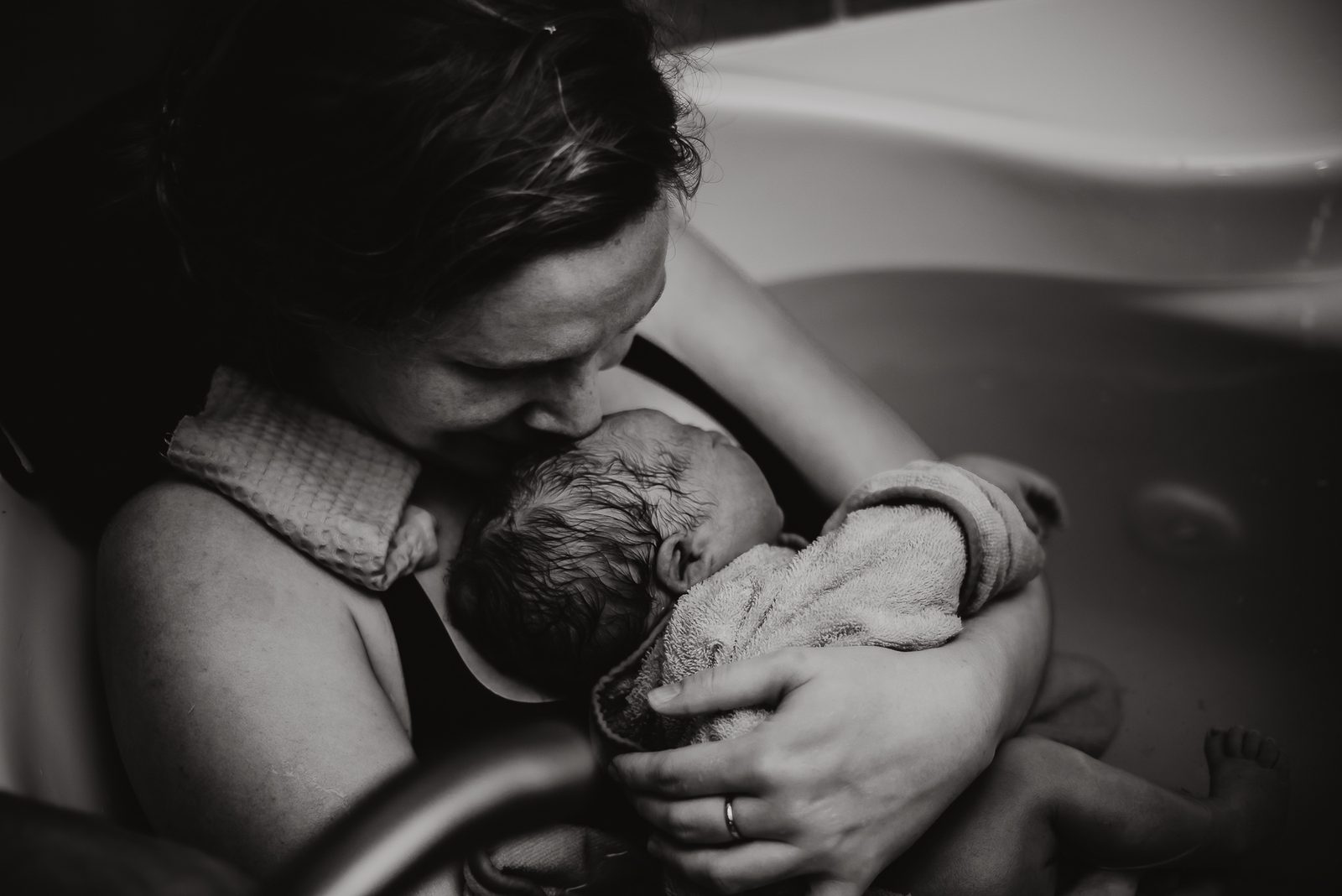 A mother holding and kissing her newborn skin-to-skin in the birth pool